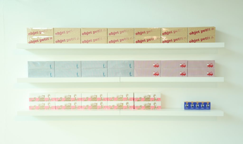 Colourful boxes, wrapped in clear plastic shrink wrap, are arranged neatly across three floating shelves.